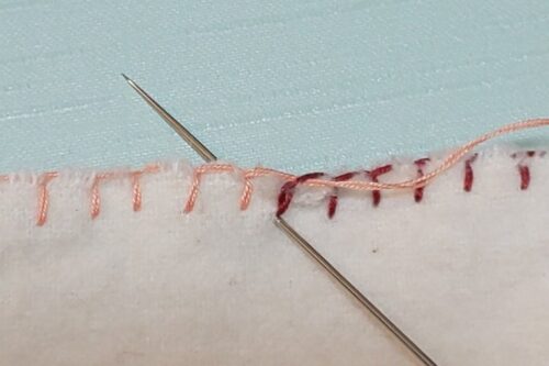 ブランケットステッチの縫いはじめの穴に後ろへ向かって針を刺している