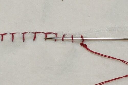 縫いはじめの玉結びを隠すためにブランケットステッチの縫い目に通した針