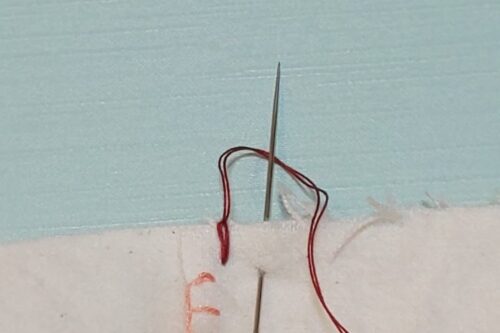 糸を引っ張ってブランケットステッチのひと針目を刺し終わり、数ミリ隣に針を刺している。