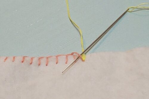 ブランケットステッチの縫い終わりの目に、新しい糸の針を後ろから通す