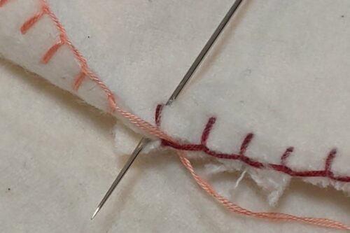 縫いはじめの穴に針を刺して、２枚の生地の間に針を出している。